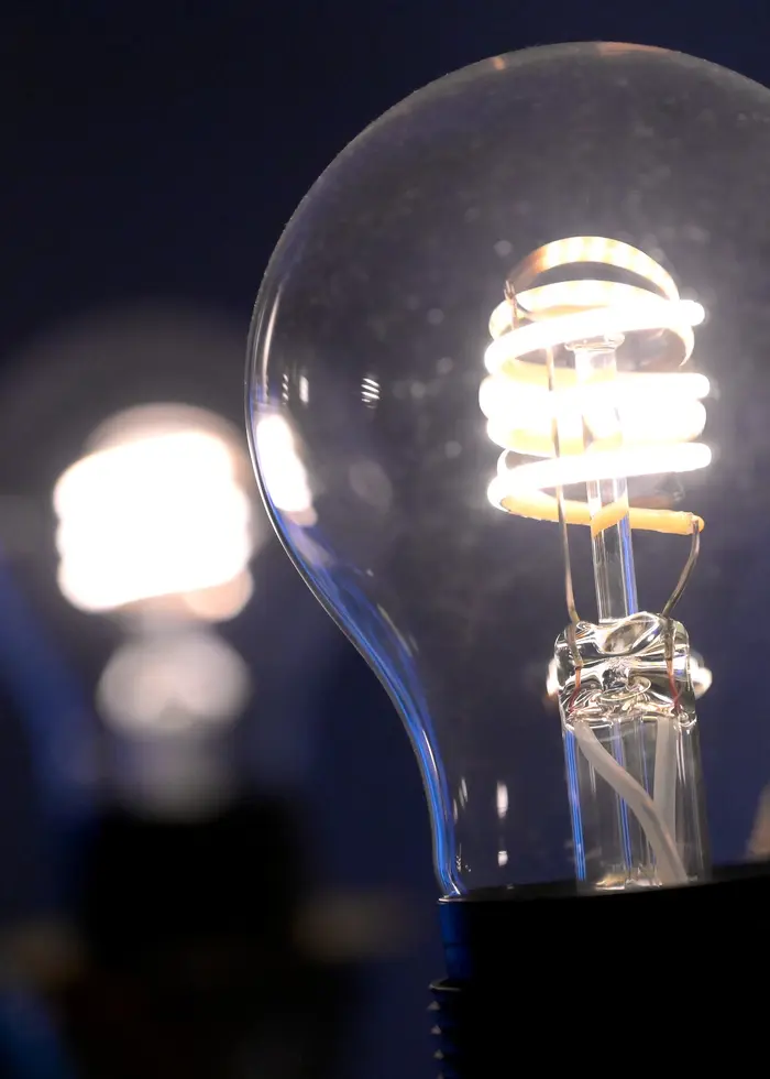 En svart sladd är inkopplad i ett jordat 230-volts eluttag på en vit vägg. Sladden ligger på ett trägolv och är delvis ihoptrasslad.