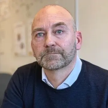 Marcus Walldén (M), ordförande för barn- och utbildningsnämnden, sitter vid ett konferensbord i ett kontorsrum med en vit tavla och en väggmålning i bakgrunden.