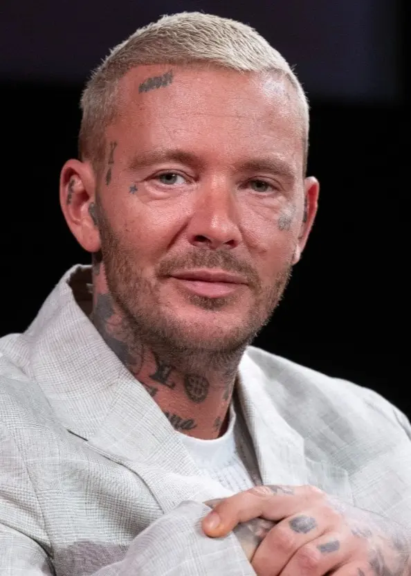 Joakim Lundell syns i en grå kavaj med snaggat och blonderat hår. Han har tatueringar på händerna, halsen och i ansiktet. Två skärmdumpar är inklippta över bilden som visar videos från sociala medier. 