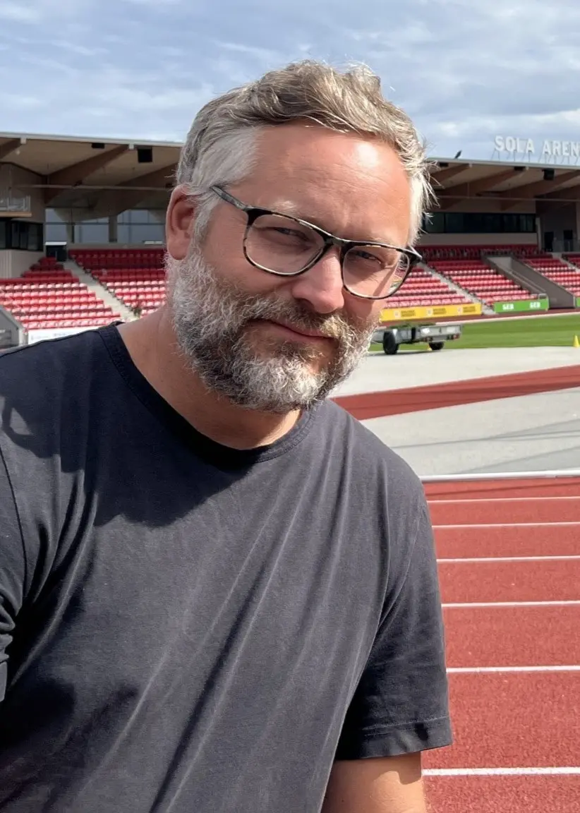 Johan Engberg, en av arrangörerna för SM i friidrott i Karlstad och Kil samt IF Götas klubbchef, sitter vid en friidrottsarena med löparbanor och läktare i bakgrunden.