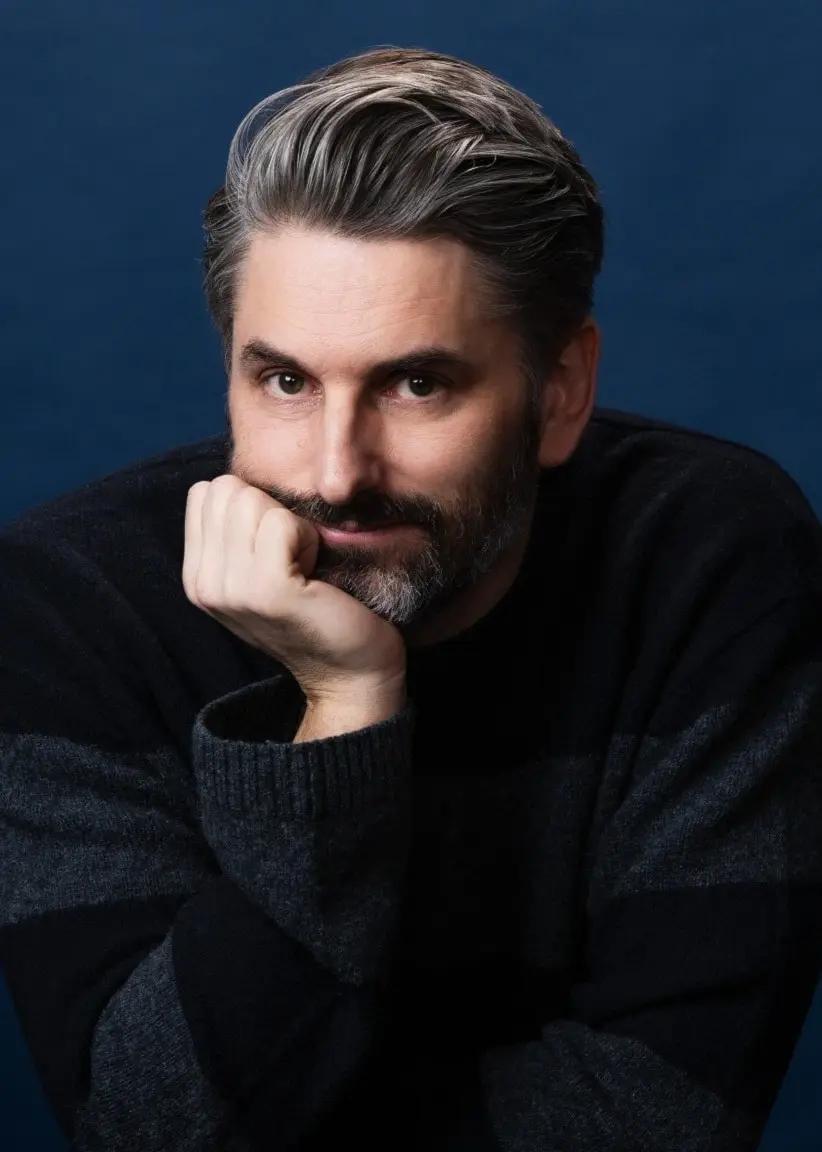 Portättfoto på förfataren Andrev Walden som lutar huvudetmöt höger hand och tittar in i kameran. 