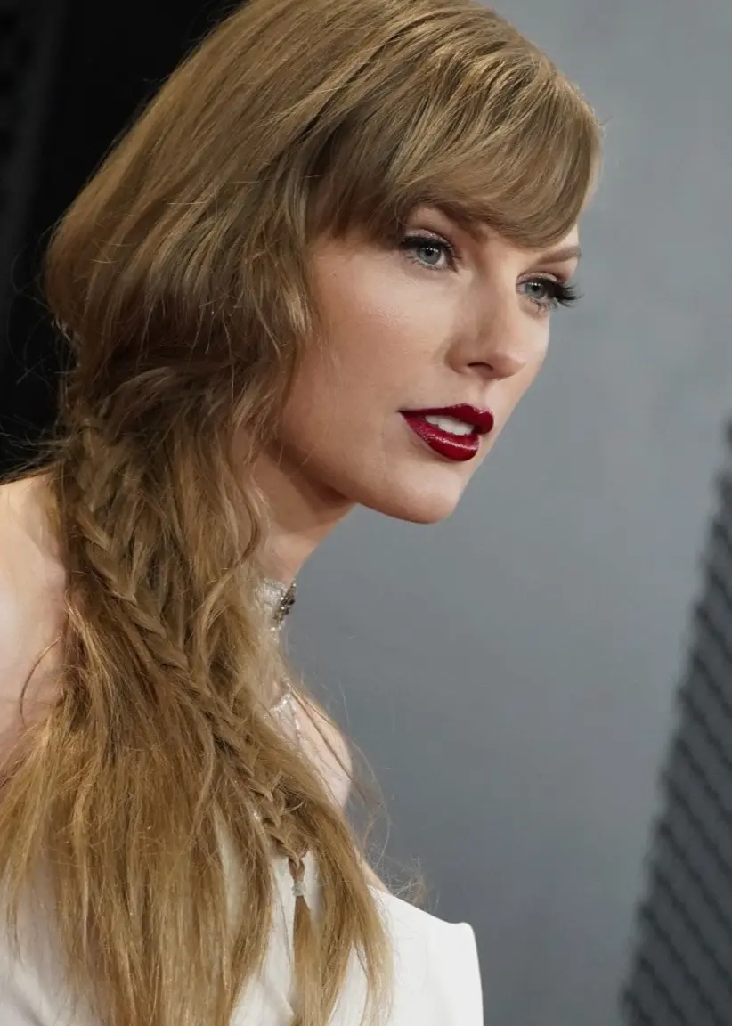 Taylor Swift ses i en vit klänning med svart detalj på axeln vid Grammy Awards, med en bakgrund av geometriska mönster och Grammy-logotypen.