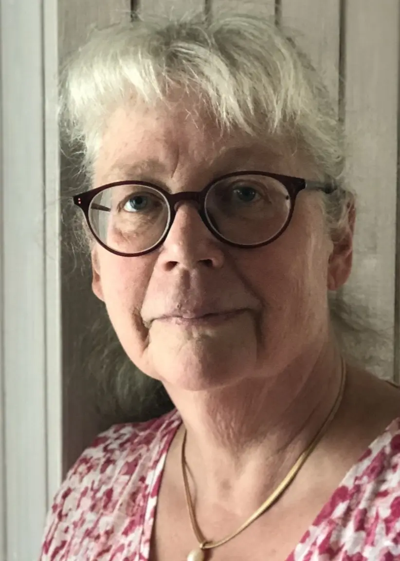 Kvinna med ljust hår och glasögon mot en trävägg