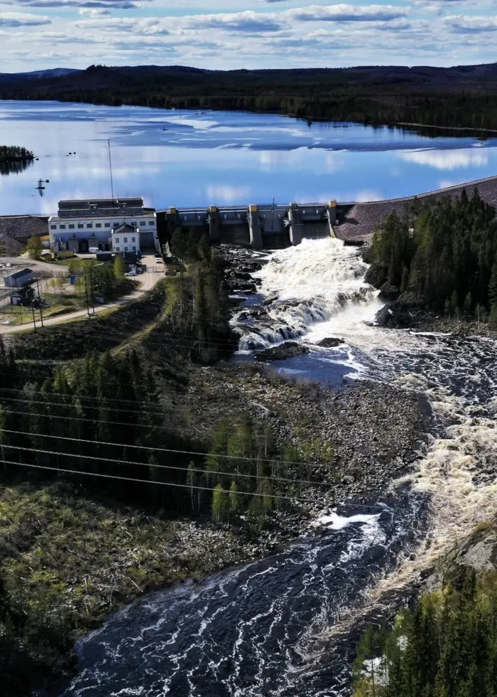 Flygbild över Laforsens kraftverk vid Ljusnan nära Kårböle. Vattnet forsar fram genom skogen mot kraftverket, omgiven av tät grönska och en spegelblank sjö i bakgrunden.