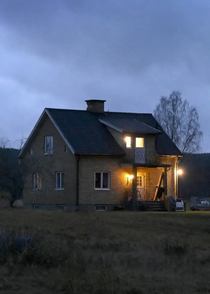 Ett ensamt hus med tända fönster och veranda står i skymning på landsbygden.