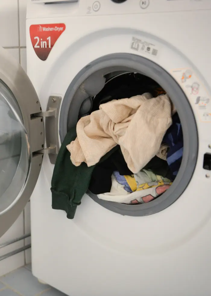 Person fyller en torktumlare med kläder i en modern tvättstuga. Torktumlaren och tvättmaskinen är energikrävande vitvaror.