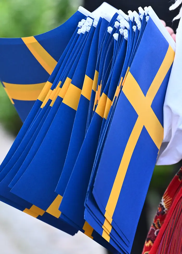 En ensam kvinna sitter på en bänk på en badbrygga vid vattnet i Huvudsta, med utsikt mot Tranebergsbron och Minneberg. Vattnet är stilla och reflekterar omgivningen under en klar dag.
