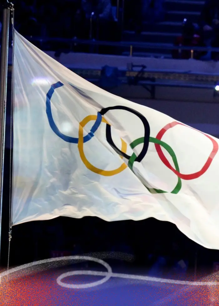 Den olympiska flaggan och Rysslands flagga vajar sida vid sida under avslutningsceremonin för vinter-OS i Sotji 2014. Bakgrunden visar en mörk arena fylld med publik.