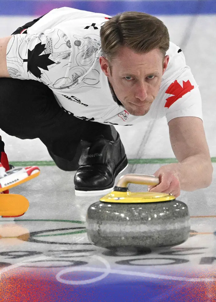 En kanadensisk curlingspelare i aktion under en gruppspelsmatch i OS 2026 mellan Schweiz och Kanada i Cortina, Italien. Personen ligger framåtlutad och styr stenen på isen med precision.