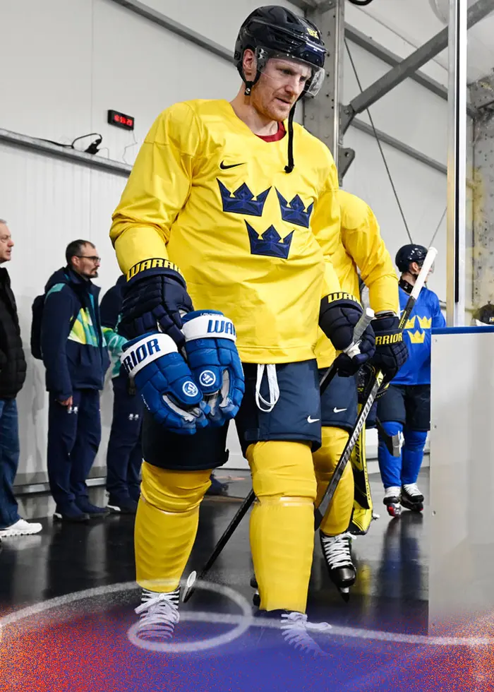 En person iklädd en svart keps och en svart tröja med texten 'SWE' sitter framför en röd trappa. På tröjan syns även logotyper, inklusive en från Uniqlo.