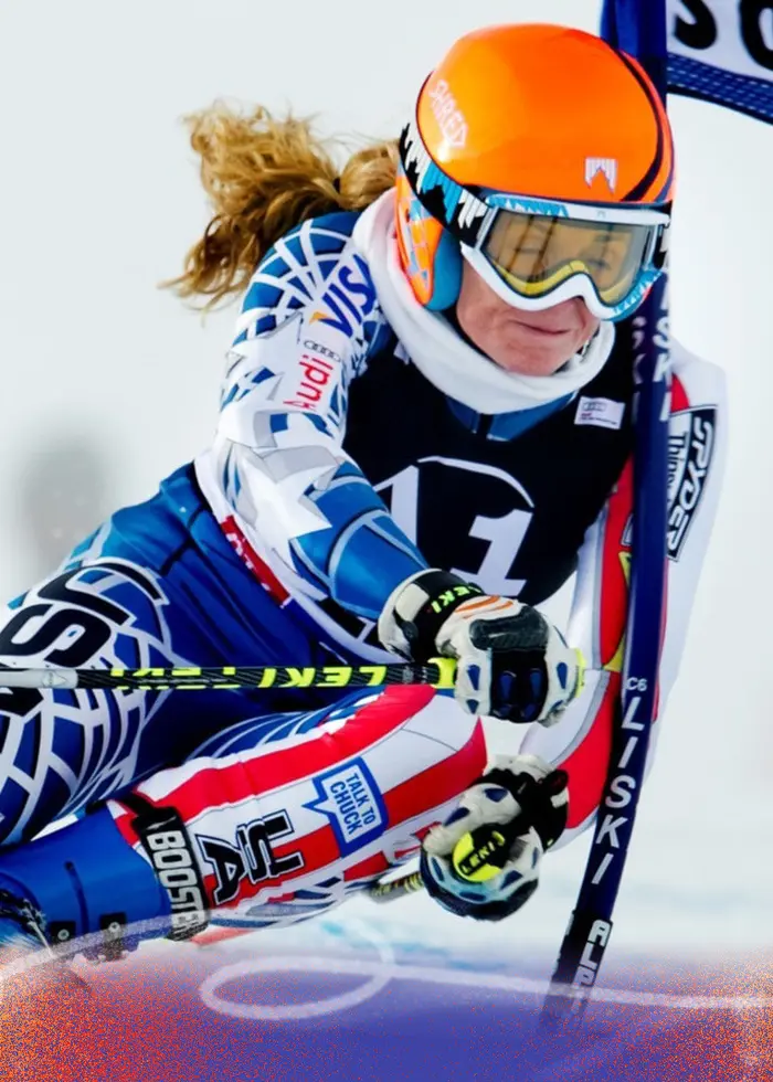 Två skidåkare tävlar i storslalom på en snötäckt bana. Den vänstra åkaren bär orange hjälm och blåvit dräkt, medan den högra åkaren har svartvit dräkt och svart hjälm.