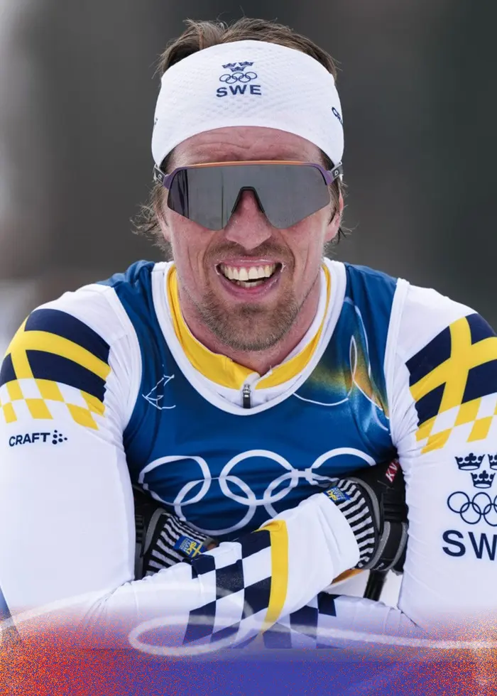 En svensk längdskidåkare i tävlingsdräkt med svenska landslagets färger och olympiska ringar synliga på bröstet åker i ett snöigt landskap under vinter-OS 2026 i Milano Cortina.