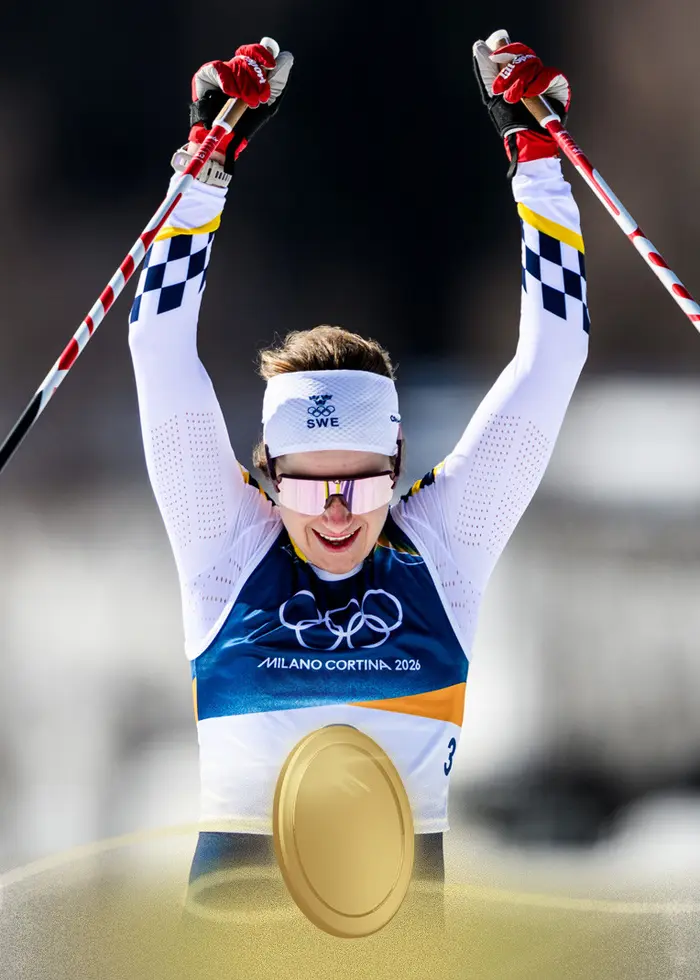 En kvinnlig längdskidåkare från Sverige tävlar i ett lopp under vinter-OS 2026 i Milano Cortina. Hon bär en vit pannband, gul och blå dräkt med startnummer 3, och håller stavar i händerna.