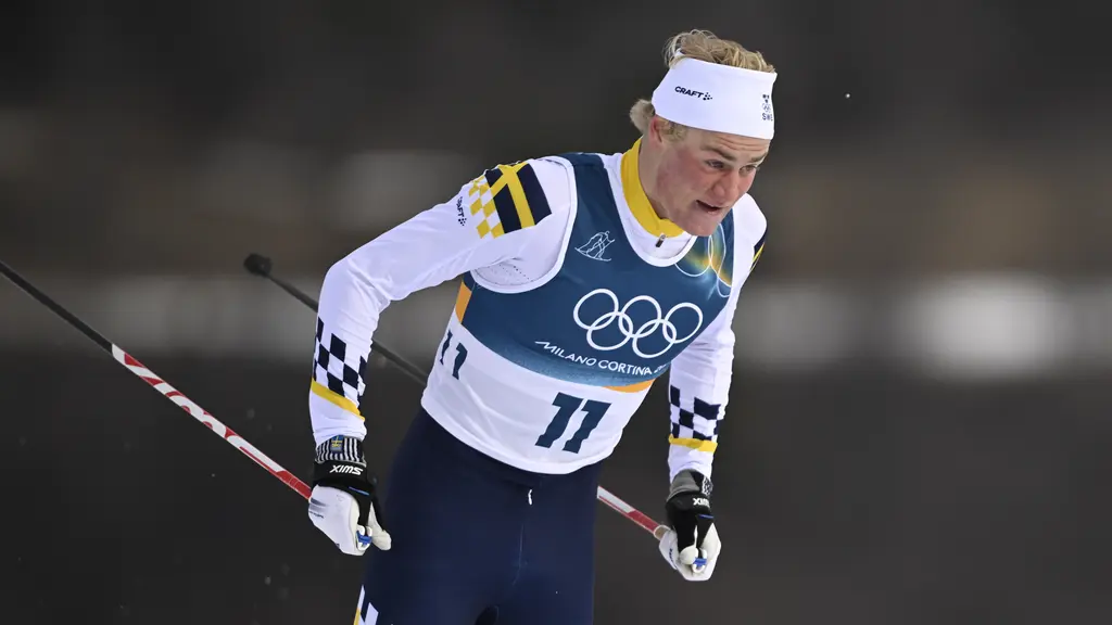 En tjej och en kille klädda i färgglada kläder, sittandes på en bänk, tittar leende på varandra. Interiör.