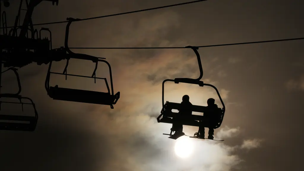 Två skidåkare är svarta siluetter i en stolslift för två personer. Himlen är mörk. Foto: 	Abbie Parr /AP/TT