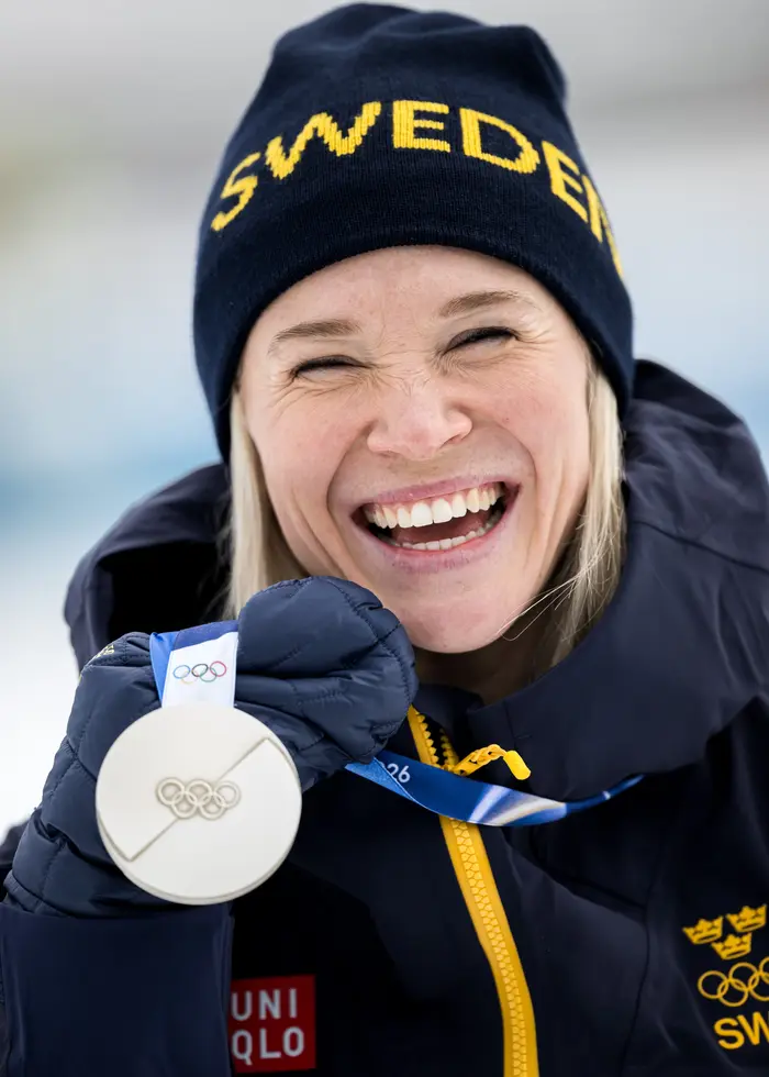 Tre längdskidåkare i vita dräkter kramar om varandra