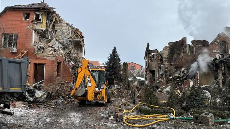 En nattlig gatubild i Lviv, Ukraina, visar skador på en byggnad efter explosioner. Fönster är krossade, och avspärrningsband markerar området. Personer inspekterar platsen för händelsen.
