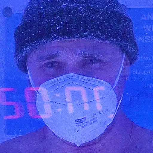 Person med mössa och munskydd i blått ljus.