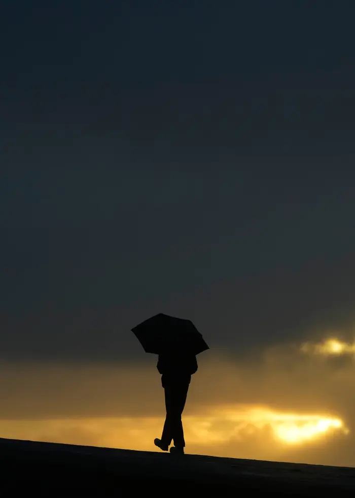 Siluett av en person gåendes med ett paraply mot en solnedgång. Foto: Jeff Chiu.