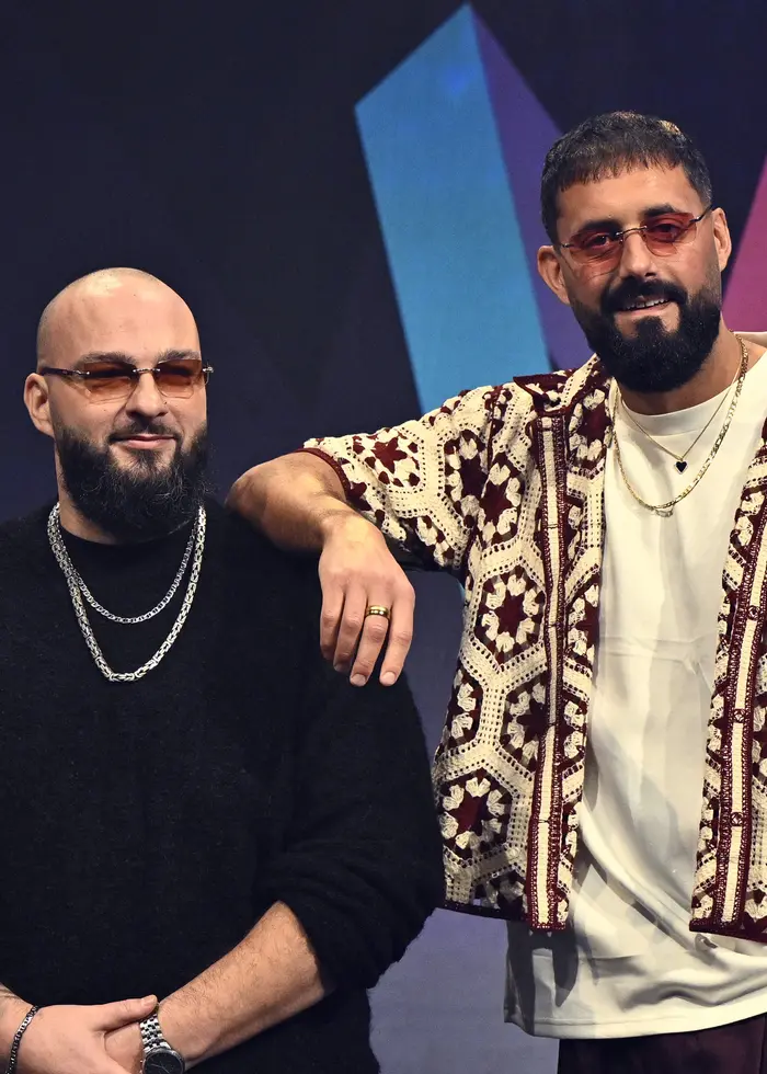 Sami Rekik och Ali Jammali i gruppen Medina står på en scen under en presskonferens i Stockholm inför Melodifestivalen 2026. Det står framför en färgglad bakgrund med geometriska mönster.