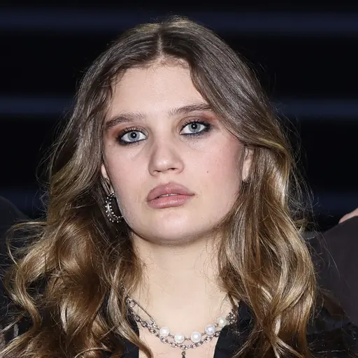 En person står framför en affisch med texten 'Nominerad' i en upplyst miljö, med fönster som visar en stadsmiljö i bakgrunden.