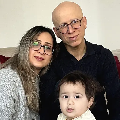 Till vänster i bild sitter Emanuel i en barnstol och håller i en barnbok. På höger sida finns en porträttbild av Shila Monjezi.