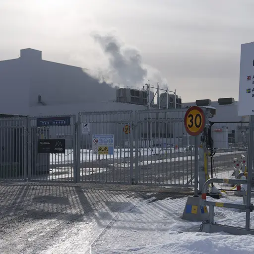 En stor vit industribyggnad vid vattnet, med ventilationssystem och rör synliga på utsidan. Byggnaden tillhör en batterifabrik i Skellefteå, tidigare ägd av Northvolt och nu övertagen av Lyten.