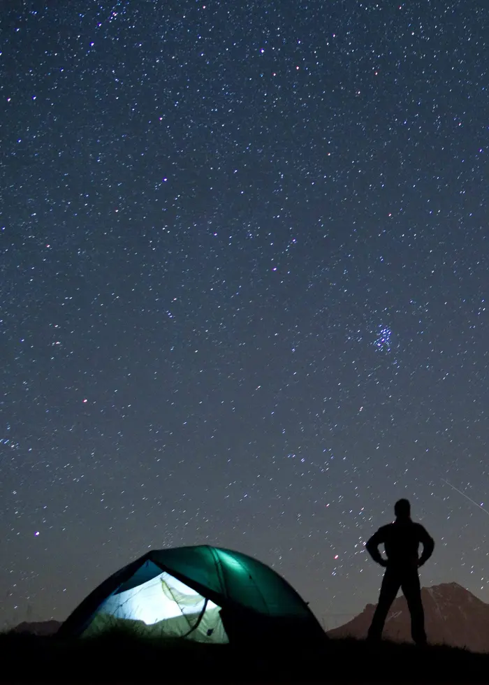 En person står bredvid ett tält och blickar upp mot en stjärnklar himmel. Foto: Alessandro Della Bella.