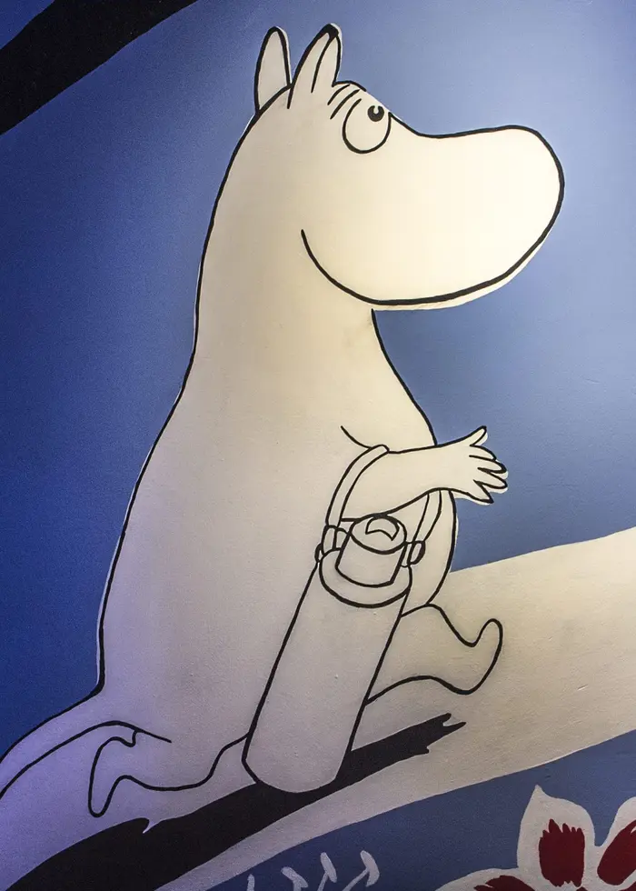 Programledare Louise Epstein sitter framför grafisk bakgrund iförd röd tröja och beige manchesterbyxor.