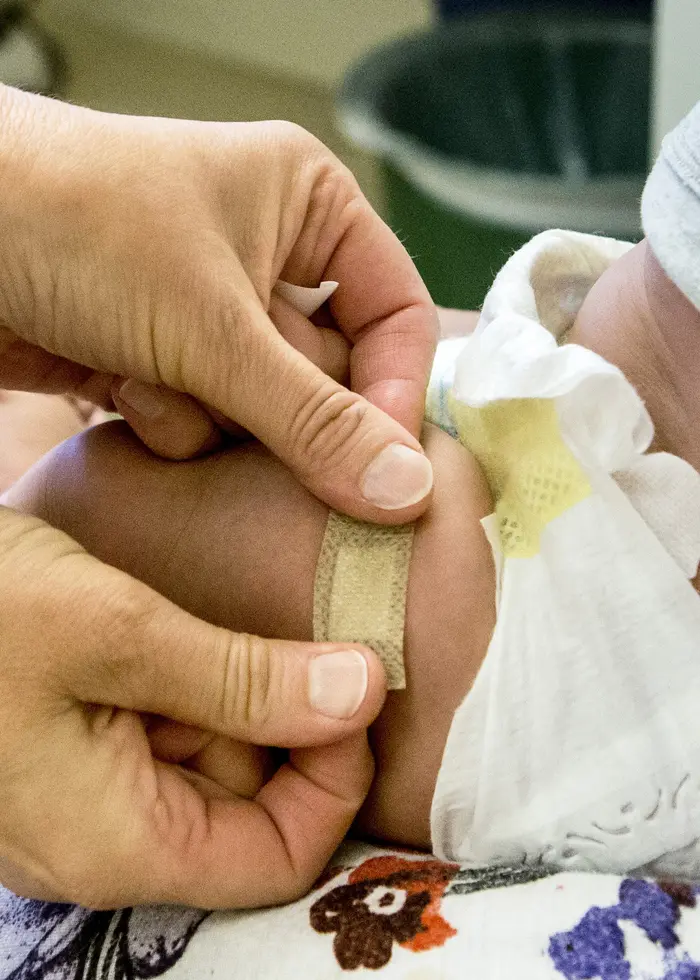 En nyfödd baby ligger insvept i en filt och hålls i famnen av en person. Bilden fokuserar på barnets lilla huvud och filtens mjuka textur. 