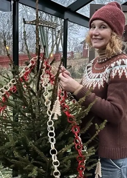 Trädgårdsmästaren Linda Schilén står i ett växthus och klär en gran fin gran i röd och vit girlang