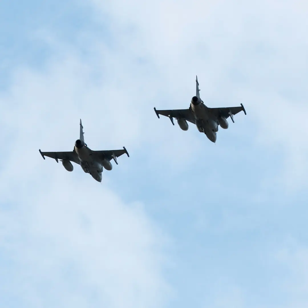 Ett stridsflygplan i luften över Thailand eller Kambodja till vänster och en nattscen med ljussken och palmer till höger, möjligen relaterat till militär aktivitet.