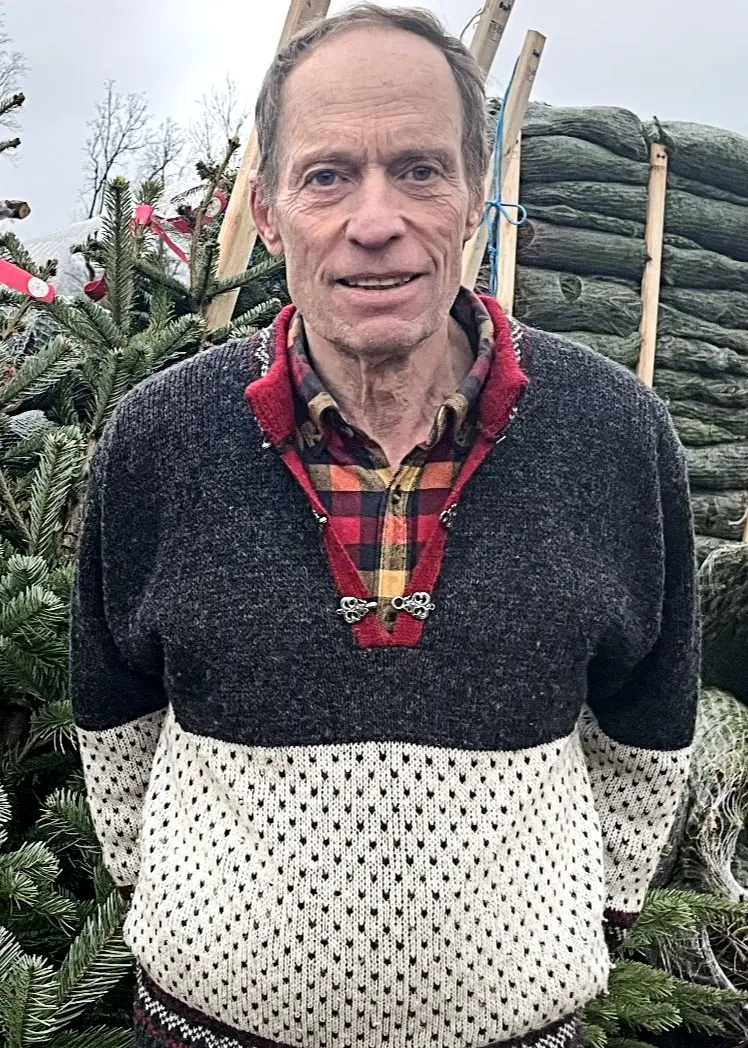 Jan Werner står med en stickad kofta bland granar.