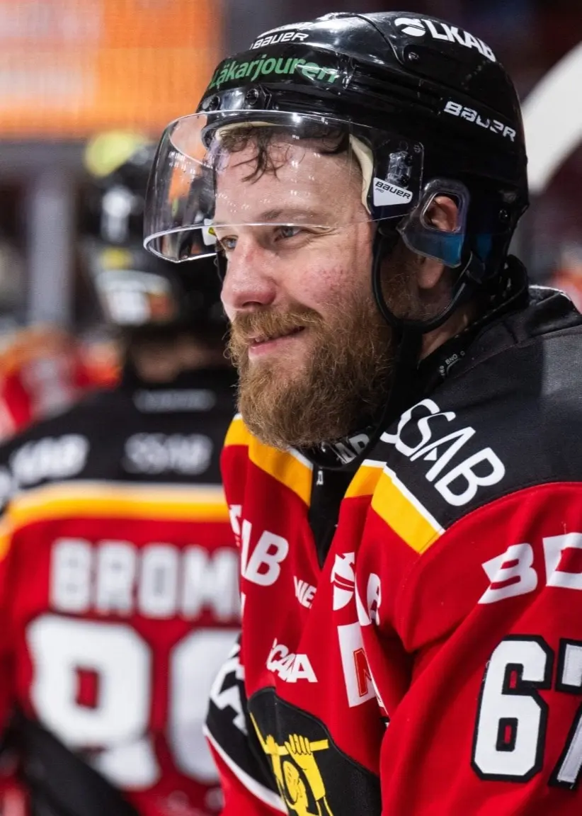 Linus Omark i en röd och svart hockeytröja med nummer 67, står vid bänken under en hockeymatch.