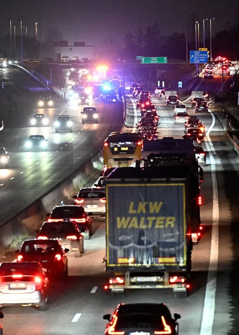 Åsa Persson, forskare vid KTH och ordförande för Klimatpolitiska rådet, står utomhus bredvid ett vitt tält. Till höger syns bilköer på en motorväg under kvällstid med blåljus i bakgrunden.