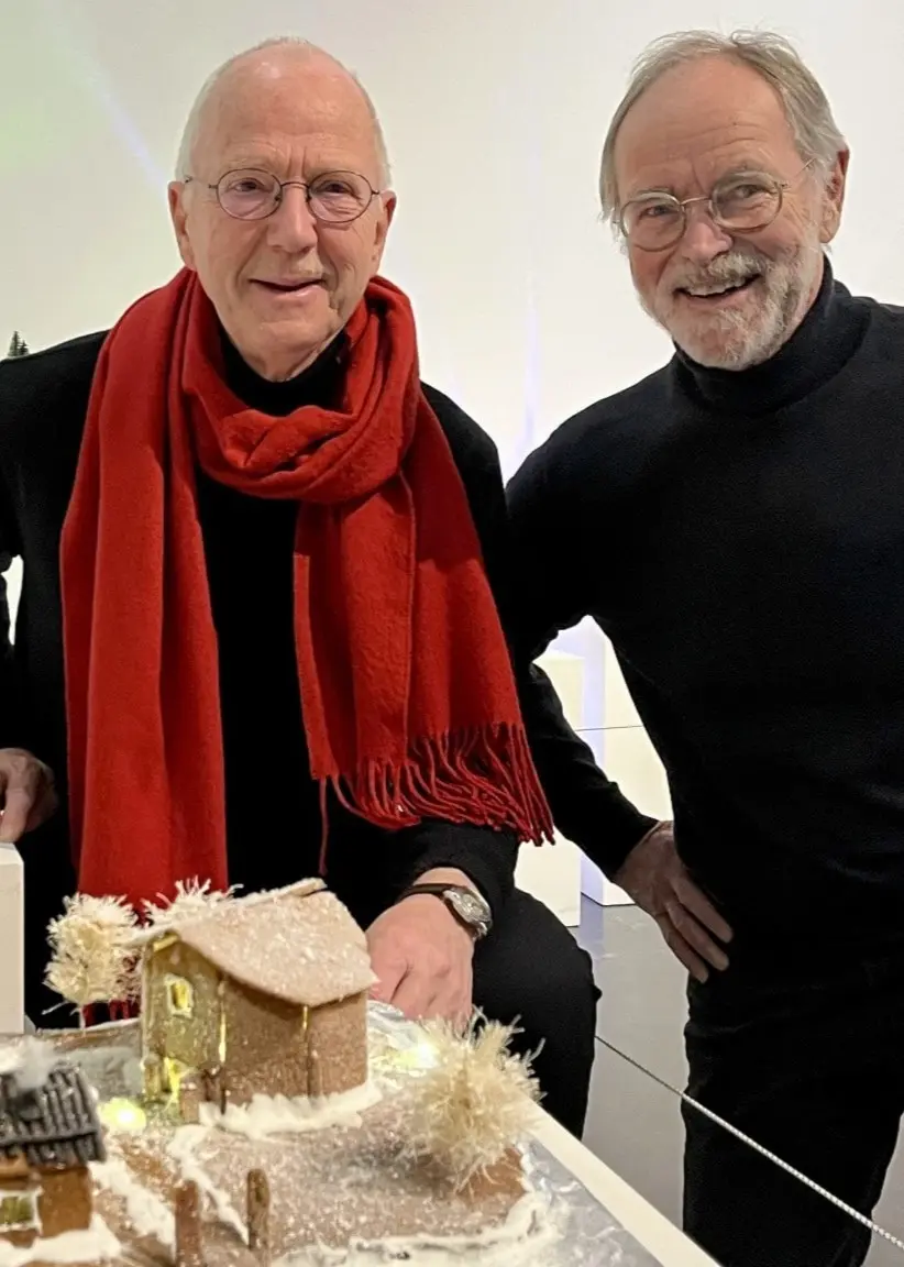 Tom Hedman och PG Thulin står framför en utställning med dekorerade pepparkakshus och figurer, inklusive färgglada detaljer och miniatyrlandskap, i en ljus inomhusmiljö.