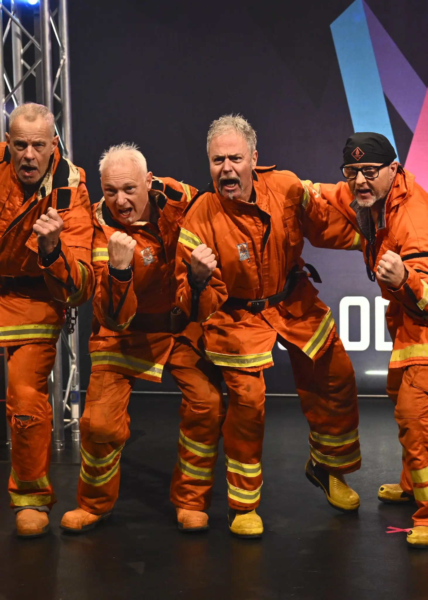 Fem män i orangea brandmanskläder, och en kvinna i grön jacka.