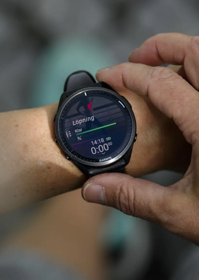 En person justerar en träningsklocka på sin handled. Skärmen visar data som pulsmätning, vilket symboliserar användning av wearables för att optimera hälsa och träning.