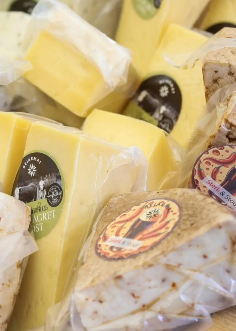Olika typer av ost, inklusive hårdost och kryddost, är presenterade på ett bord under Olavfestdagene i Trondheim. Osten är förpackad och märkt med etiketter som tydligt visar dess ursprung.