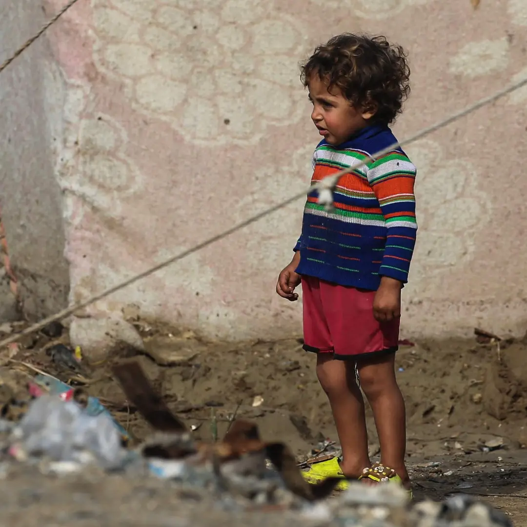 Ett litet barn står bland upphängda tygstycken som utgör ett temporärt läger på Gazaremsan.