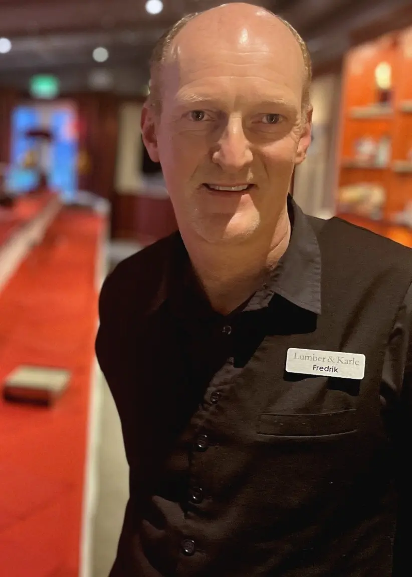 Fredrik Dufva, restaurangchef och delägare, står i en restaurang med röd dukning och dekorationer på ett långt bord i bakgrunden.