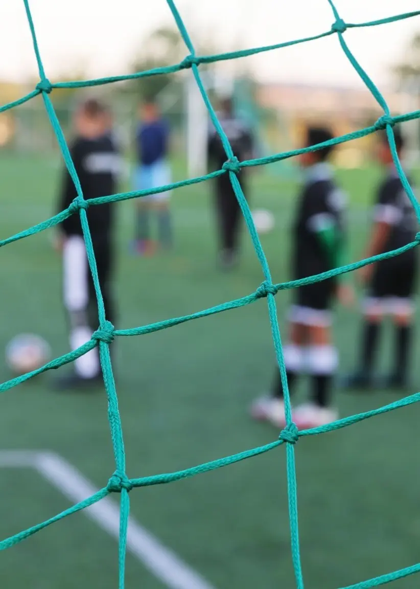 Björn Mattsson, ordförande för Ronneby bollklubb, står utomhus i en vinterjacka med bakgrund av hustak och himmel. Till vänster syns en fotbollsplan med spelare i bakgrunden och ett grönt nät i förgrunden.