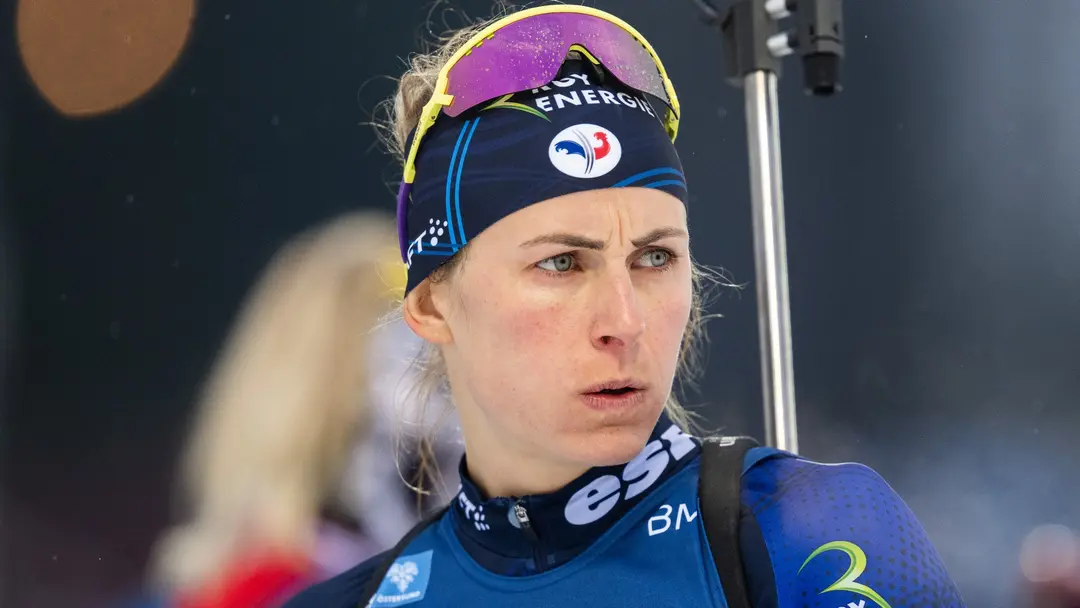 En skidåkare i färgglad tävlingsdräkt med startnummer 68 tävlar i längdskidåkning. Snö faller och bakgrunden visar en suddig vintermiljö, vilket förstärker tävlingskänslan.