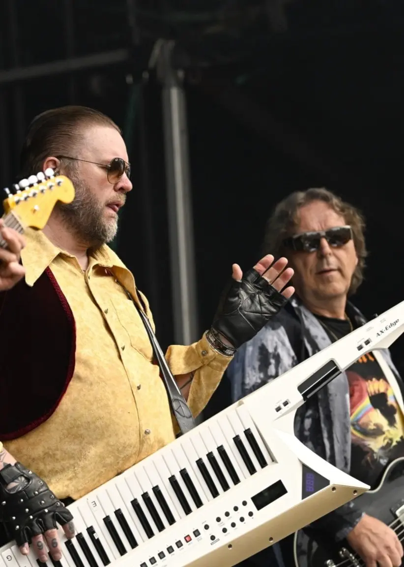 Bandet Korslagda från Älvdalen uppträder på Sweden Rock Festival. En musiker spelar elgitarr, en annan bär en keytar och en tredje spelar elgitarr på en scen utomhus.