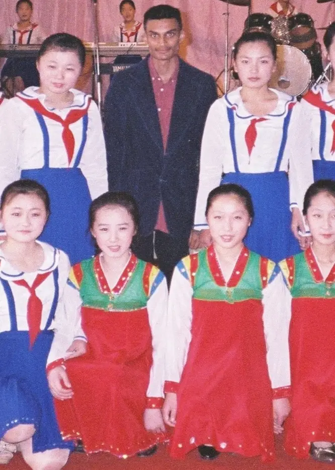 15 flickor i blo-vita dräkter står uppställda som på en klassbild. I mitten av den översta raden står Robin Jonsson med vinröd skjorta och mörk kavaj.