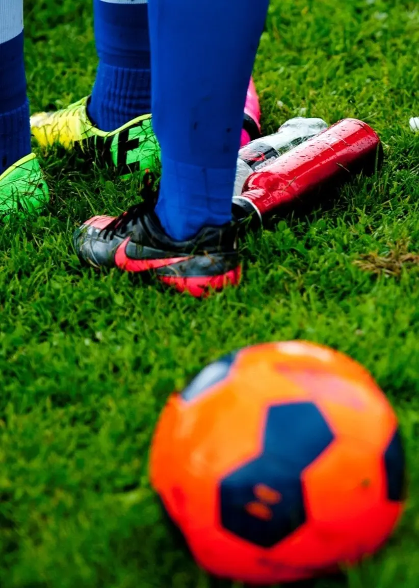 Bosse Bakken, ordförande för Skattkärrs IF, bredvid en bild av en fotbollsplan med en orange fotboll, vattenflaskor och fotbollsspelare i blå strumpor och skor.