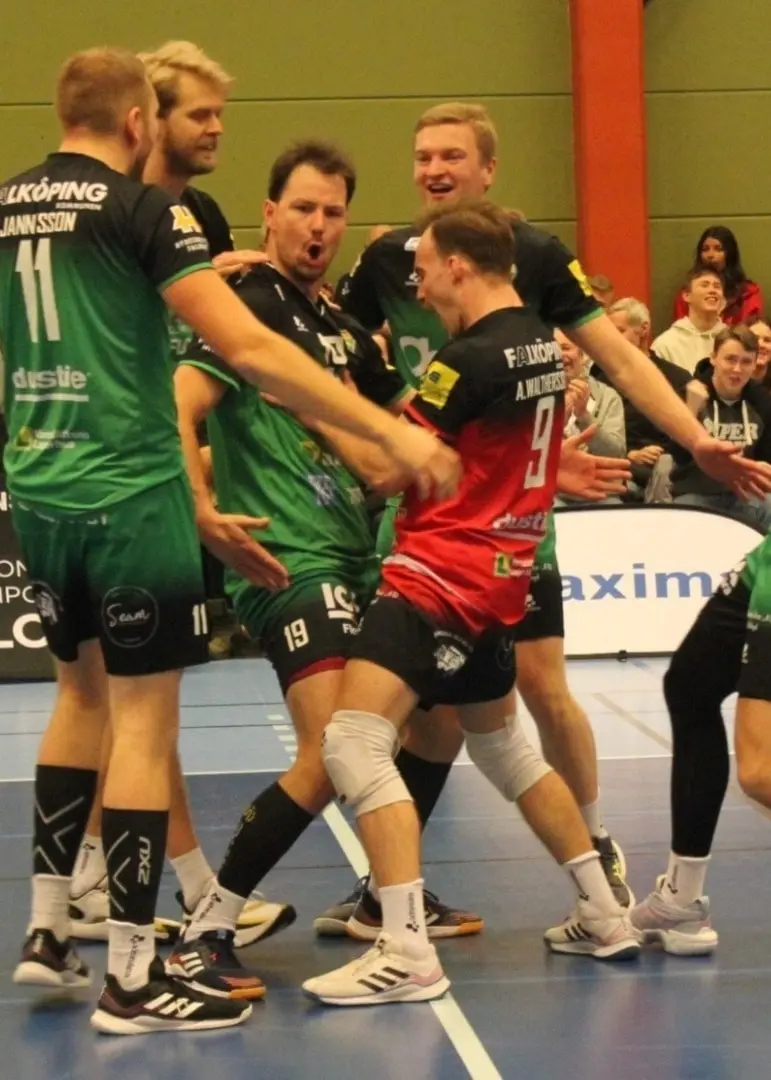 Volleybollsspelare i gröna och svarta matchkläder firar ett mål på planen, medan en person i träningskläder syns på sidan av bilden med en höjd arm och två fingrar uppsträckta.
