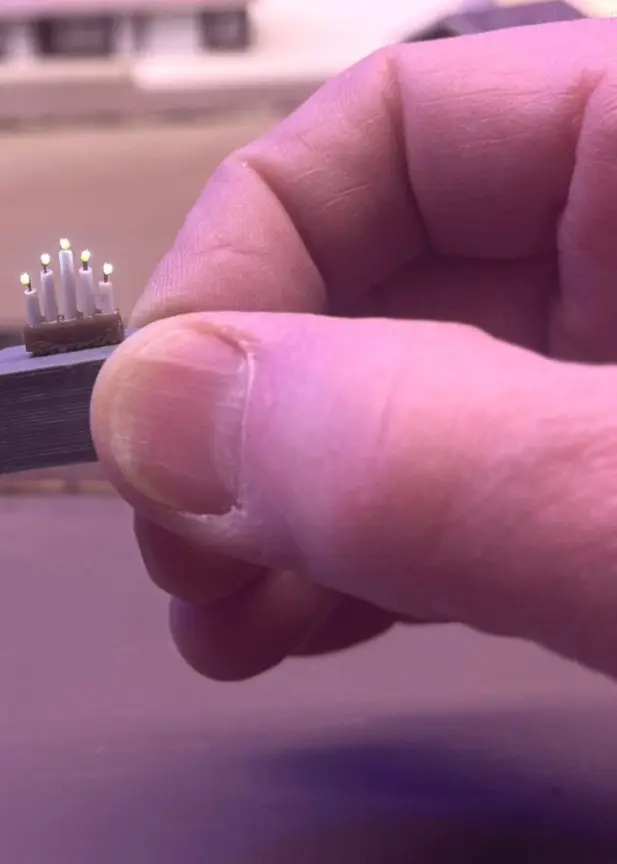 En bild uppdelad i två sektioner. Till vänster en äldre man med vitt hår i en mörk tröja, bakgrunden visar byggnader. Till höger en hand som håller en liten elektronisk komponent nära en modelljärnväg. Tommy har länets minsta stake