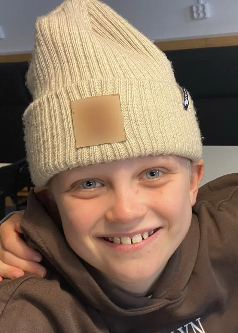 Två barn sitter bredvid varandra vid ett bord inomhus. Det ena barnet har på sig en vit stickad mössa och båda har armarna runt varandra i en vänskaplig gest.