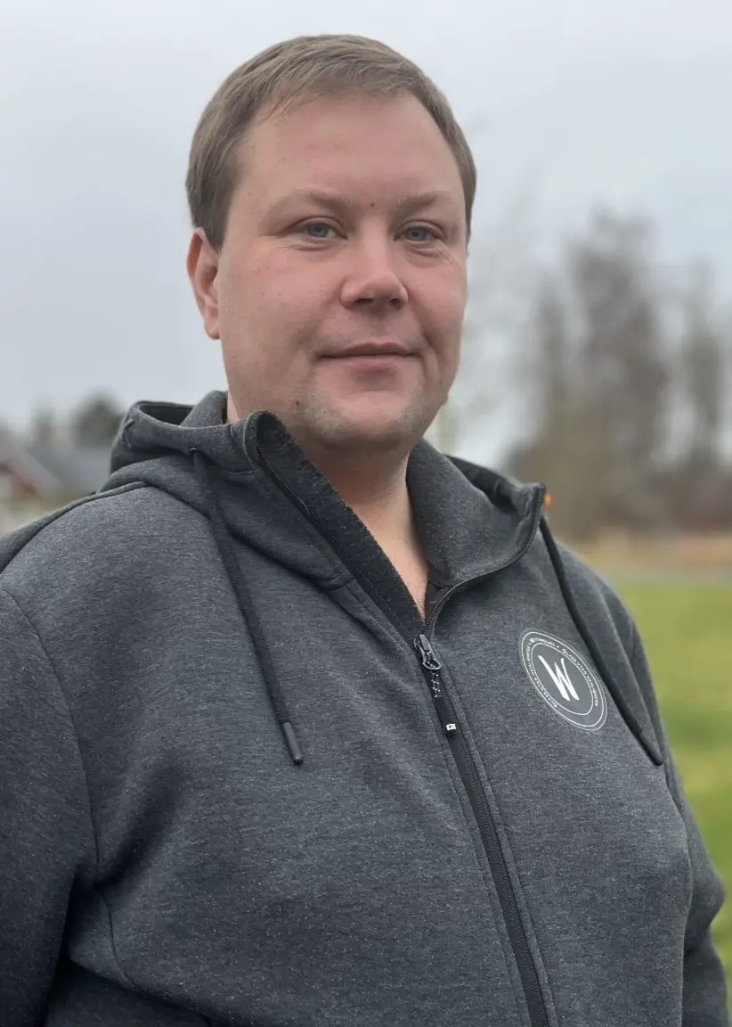 Johannes Johansson Ekfeldt står utomhus i en grå hoodie vid en grusstig. Bakom honom syns gräsmatta, träd och ett vägskylt med texten 'Centrum' samt några hus i bakgrunden.